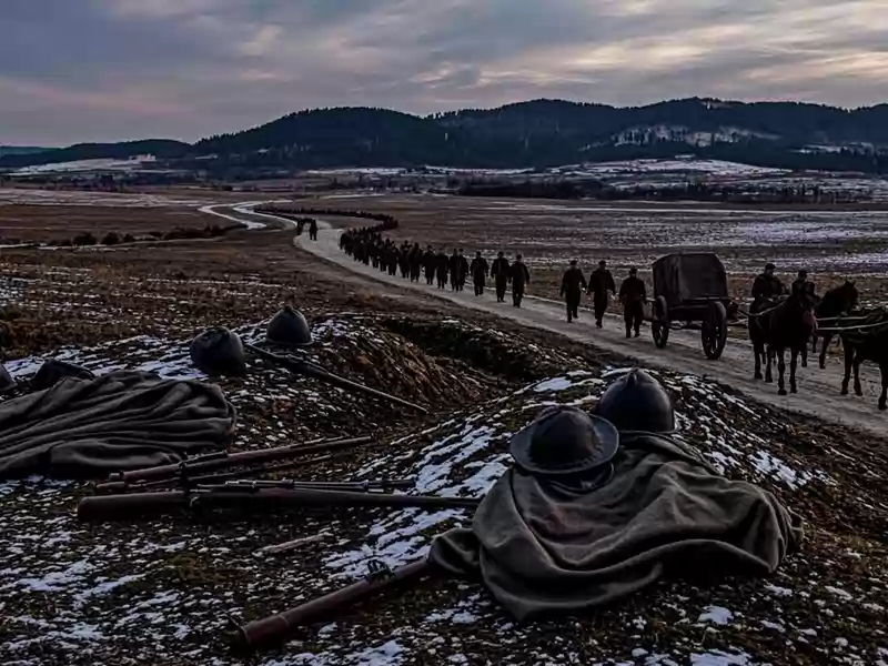 Puške, šlemovi i kaputi leže u retkom snegu na brdu, a u daljini putem kroz polja odlazi duga kolona ljudi i zaprežnih kola ka šumovitim brdima u sumrak.